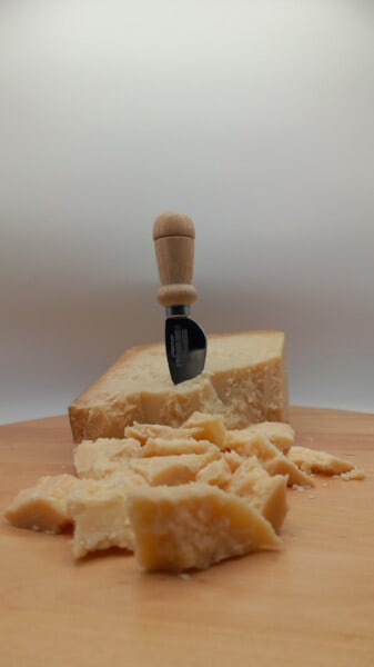 Punta di Parmigiano Reggiano con scaglie in primo piano e coltellino scagliatore da formaggio